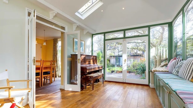 Amplia habitación con piano, comedor y un gran ventanal con vistas al jardín.