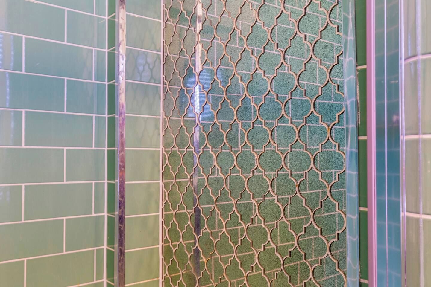 Une salle de bain avec des carreaux aux motifs verts et bleus et un paravent décoratif en métal.