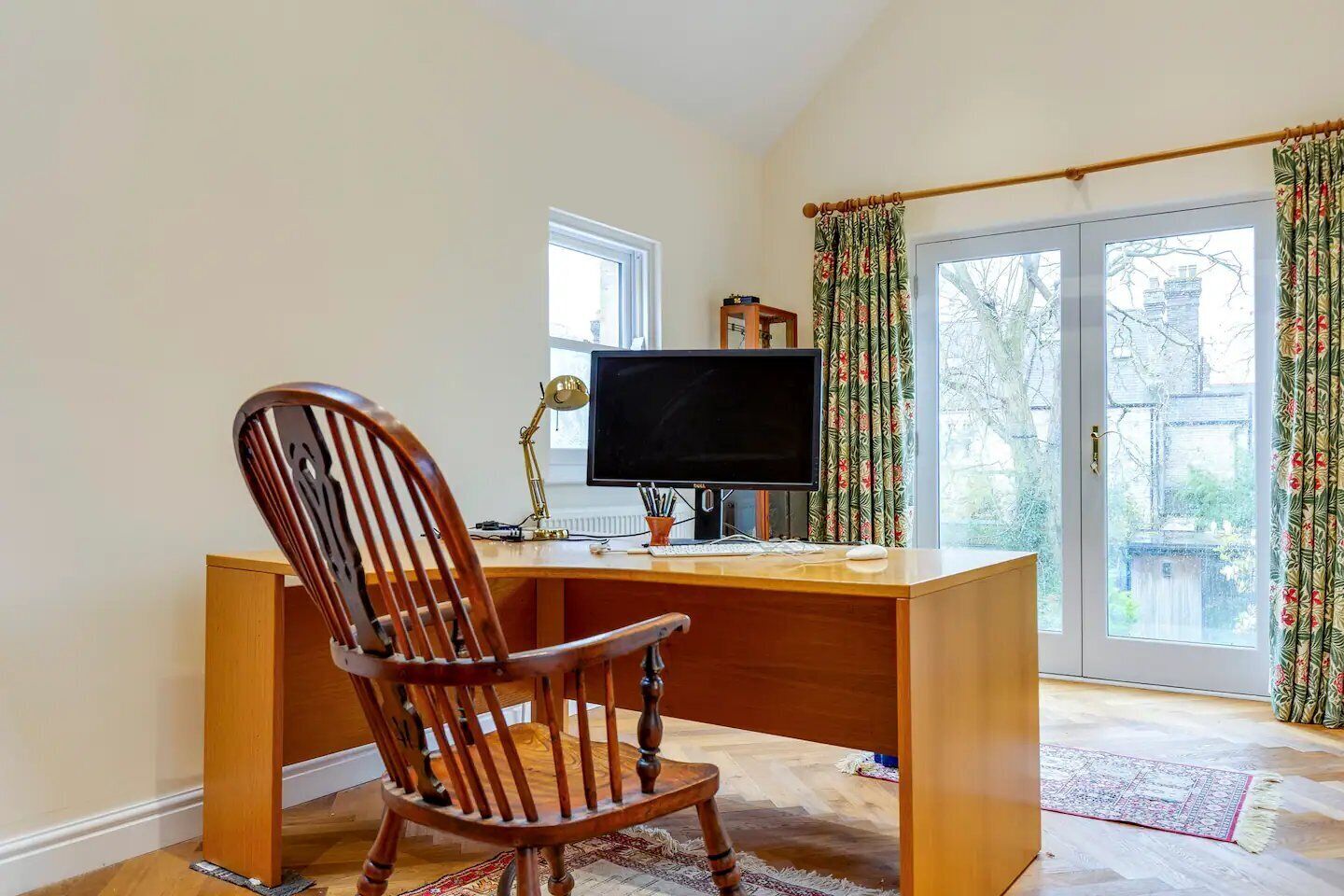 Un escritorio de madera con un monitor de computadora, una silla y una ventana con cortinas.