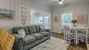 A living room with a gray sofa, white dining table, and chairs. There are framed pictures on the walls and a ceiling fan. - Sunset Rentals | Beachgate at Starfish 9 Dr. (Hilton Head Island)