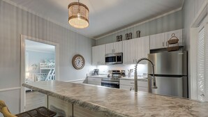 A modern kitchen with a marble countertop, stainless steel appliances, and wicker chairs. - Sunset Rentals | Beachgate at Starfish 9 Dr. (Hilton Head Island)