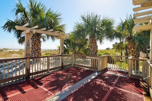 A covered outdoor area with a wooden pergola and metal safety railings, surrounded by palm trees and sandy ground. - Sunset Rentals | Evian 175 | Dog Friendly (Hilton Head Island)