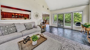 Ein geräumiger Wohnbereich mit grauem Sofa, einem Couchtisch mit Pflanze und Blick auf eine Küche sowie eine Terrasse durch große Fenster.