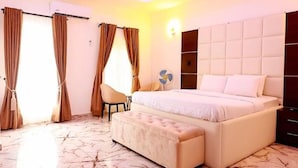A bedroom with a large bed, a bedside table, a chair, and a fan. - Exclusive 3-bed Apartment in Lagos (Lekki)