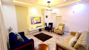 A living room with a TV, sofas, a coffee table, and a ceiling light fixture. - Exclusive 3-bed Apartment in Lagos (Lekki)