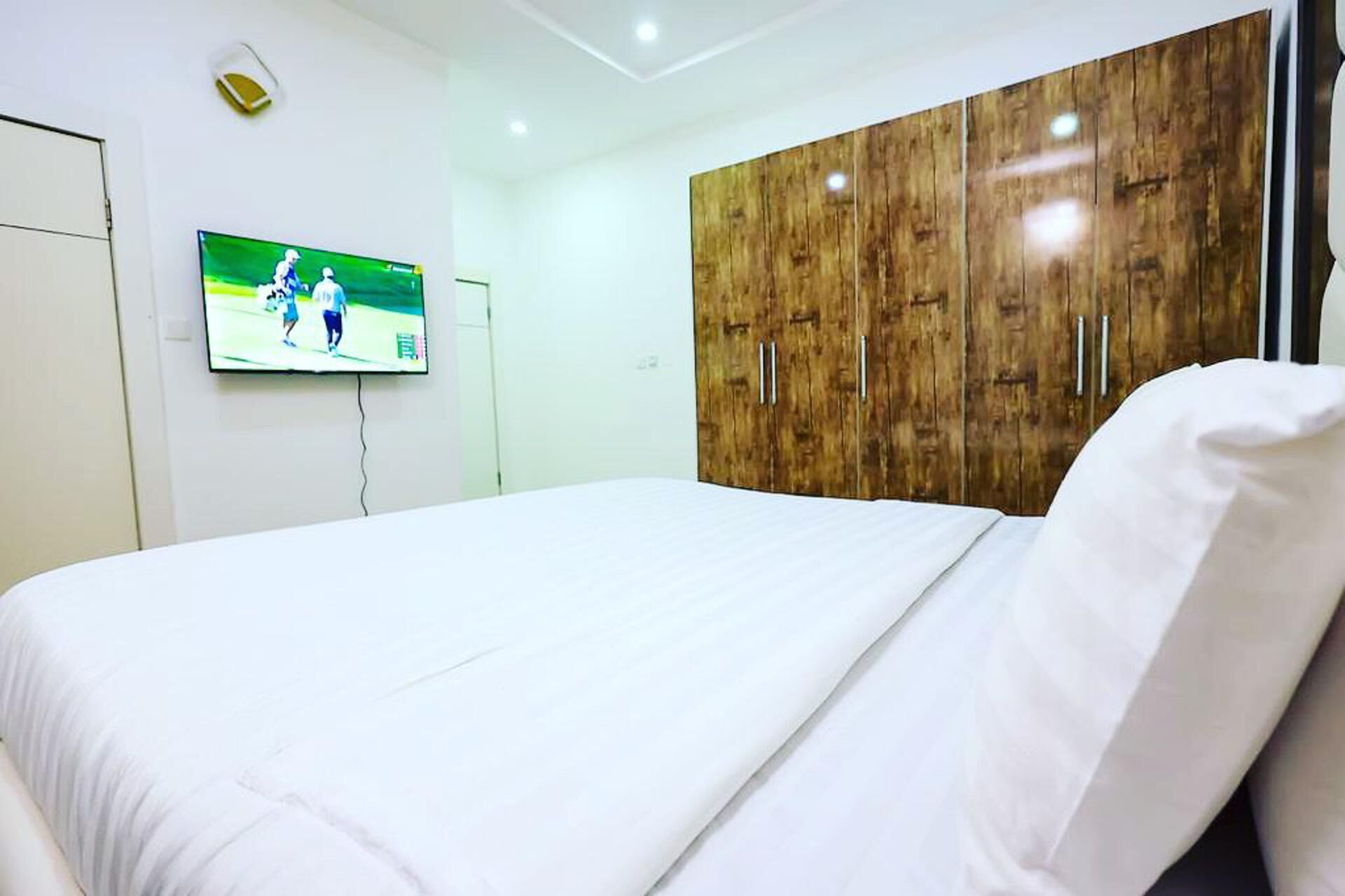 Een hotelkamer met een bed, een aan de muur bevestigde televisie en houten kledingkasten.