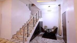 A modern interior with a marble staircase, a dining area with two chairs, and a ceiling light fixture. - Exclusive 3-bed Apartment in Lagos (Lekki)