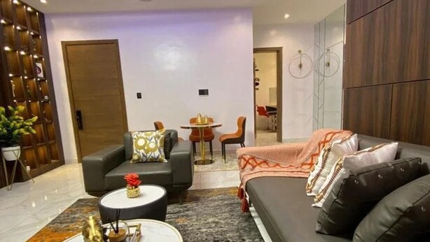 A modern living room with a sofa, coffee table, and a dining area with a table and chairs. - Exclusive 3-bed Apartment in Lagos (Lekki)