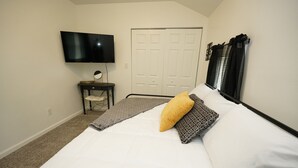 A bedroom with a bed, a television mounted on the wall, a desk with a chair, and a closet. - Entire 2 Bedroom Home (Elyria)