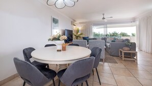 Ein stilvolles Wohnzimmer mit einem runden Esstisch, grau gepolsterten Sesseln, einem grauen Sofa und einem Deckenventilator.