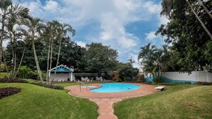 Ein Garten mit Pool, überdachter Sitzgelegenheit und einem Kiesweg.
