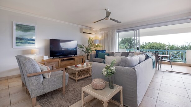 Ein modernes Wohnzimmer mit Sofa, Sessel, Fernseher und einem Balkon mit Blick.