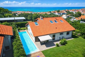 Una casa con piscina, techo de tejas rojas y vista al mar.