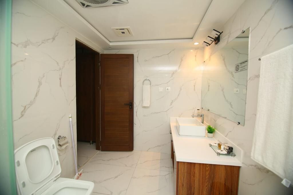 Un bagno con un WC bianco, una porta in legno, un lavandino bianco con uno specchio sopra e un pavimento in marmo.