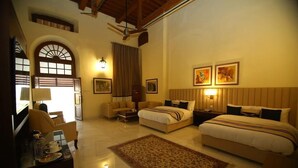 A hotel room with two beds, a sofa, a dining table, and a large window with curtains. - Peshawar Barracks Estb 1867 (Peshawar)