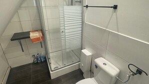 A bathroom with a glass shower enclosure, a toilet, and a small shelf with cleaning supplies. - Gemütliche 2-zimmer Wohnung in Lübeck (Lübeck)