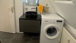 A compact laundry room with a Bosch washing machine, a small countertop with a pan, and a mirror above the sink. - Gemütliche 2-zimmer Wohnung in Lübeck (Lübeck)