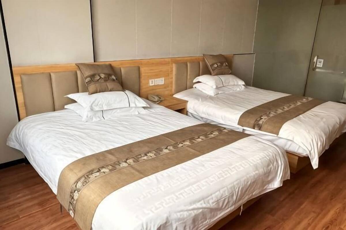 A hotel room with two beds, wooden headboards, beige walls, and a wardrobe.