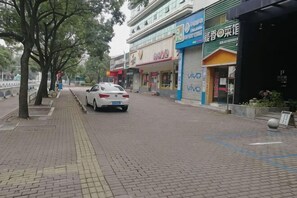 Una calle pavimentada con tiendas, un coche blanco estacionado y árboles bordeando la acera.