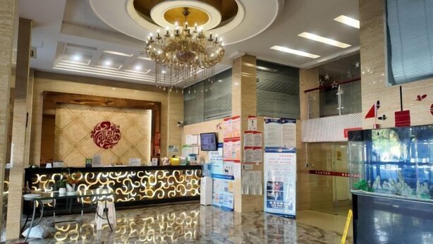 A hotel reception area with a modern chandelier, a reception desk with a patterned backdrop, and informational posters on the walls. - 0576 Business Hotel (Taizhou)