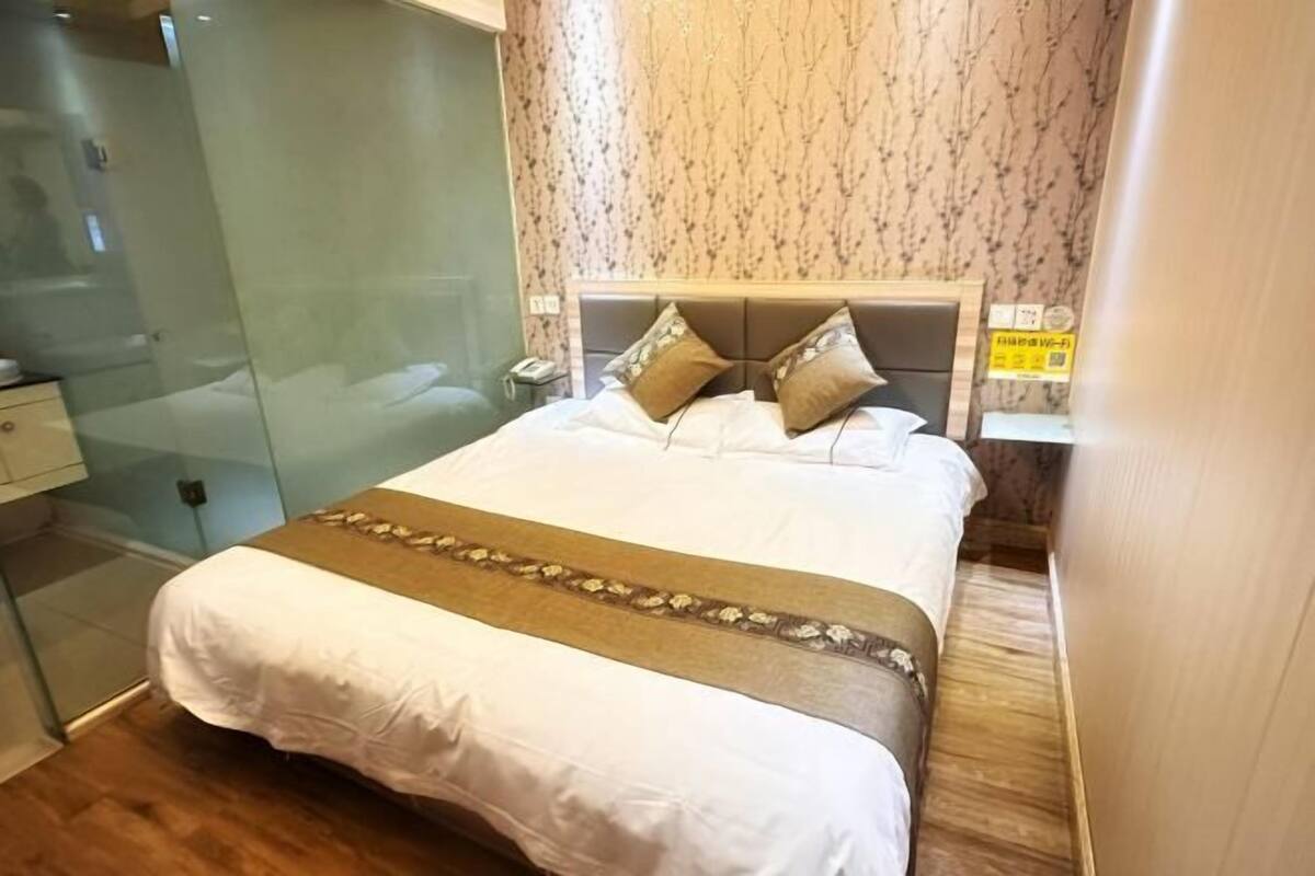 A hotel room with a bed, a glass shower enclosure, and a wooden floor.