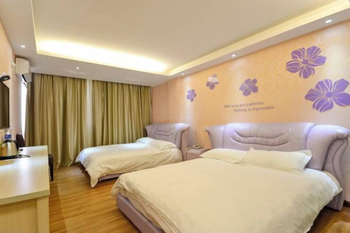 A hotel room with two beds, a desk, and a wall with floral decorations.
