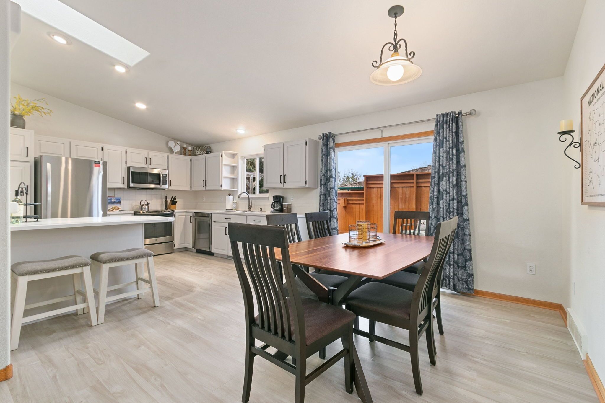 A modern kitchen with white cabinets, a stainless steel refrigerator, and a wooden dining table with chairs.