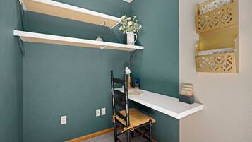 Una habitación de esquina con paredes color turquesa, un escritorio blanco, una silla negra y un estante blanco con un jarrón de flores.