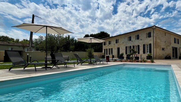A swimming pool with lounge chairs and umbrellas, a stone building in the background, and a partly cloudy sky. - Le Repaire de Maltus "gîte & Spa (Lussac)