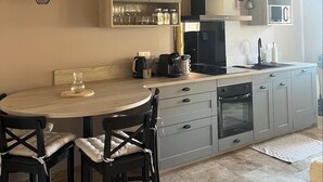 A modern kitchen with wooden beams, grey cabinets, a round dining table, and black chairs. - Le Repaire de Maltus "gîte & Spa (Lussac)