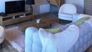 A cozy living room with a wooden ceiling, a flat-screen TV, a sofa, and a chair. - Le Repaire de Maltus "gîte & Spa (Lussac)