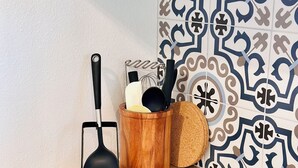 A kitchen counter with a black induction cooktop, a black spatula, a wooden container holding kitchen utensils, and a patterned backsplash. - Santorini Cabana in Zephyrhills (Zephyrhills)
