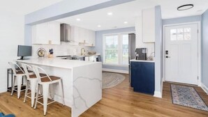 Una cocina moderna con gabinetes blancos, una isla de mármol y una zona de bar con sillas blancas.