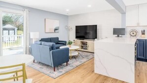 Una sala de estar moderna con un sofá, televisor y una zona de cocina con armarios y una encimera.