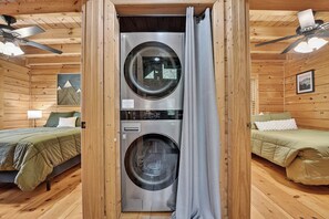 A compact room with two beds, a washing machine, and a ceiling fan.