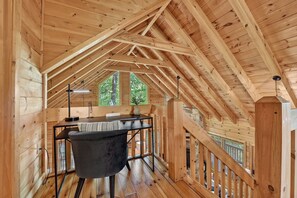 A wooden interior with a high ceiling, a desk with a chair, and a window with a view of trees.