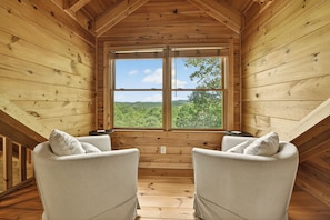 A wooden cabin with a large window offering a view of a forested landscape.
