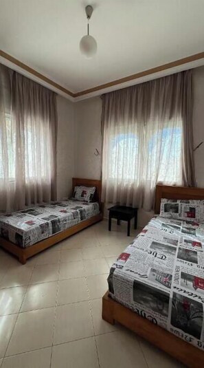 Two single beds with patterned bedding, a small table, and a tiled floor.