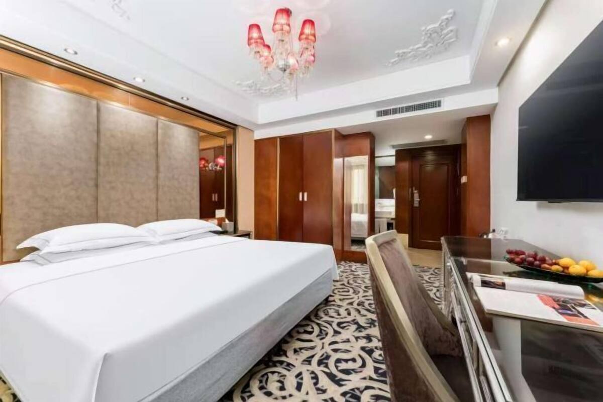 A hotel room with a large bed, a desk with a mirror, and a chandelier.