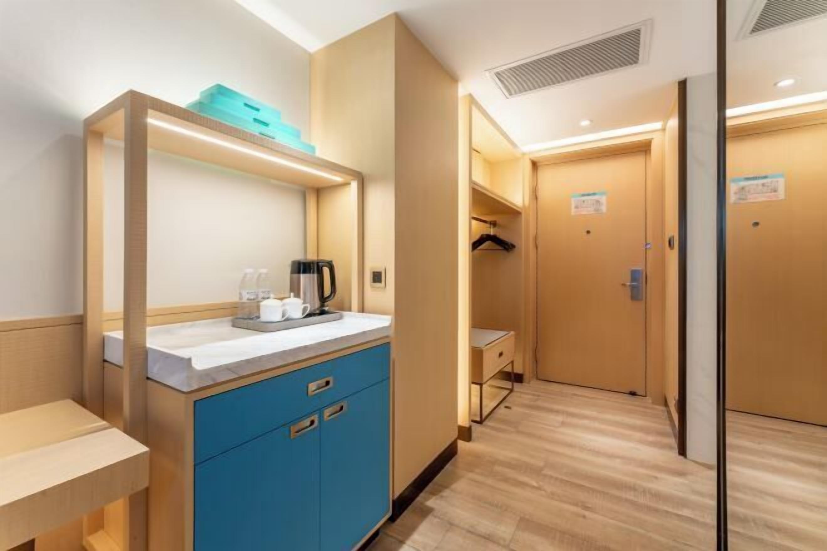 A hotel room with a kitchenette, a small table, a blue cabinet, and a wooden floor.