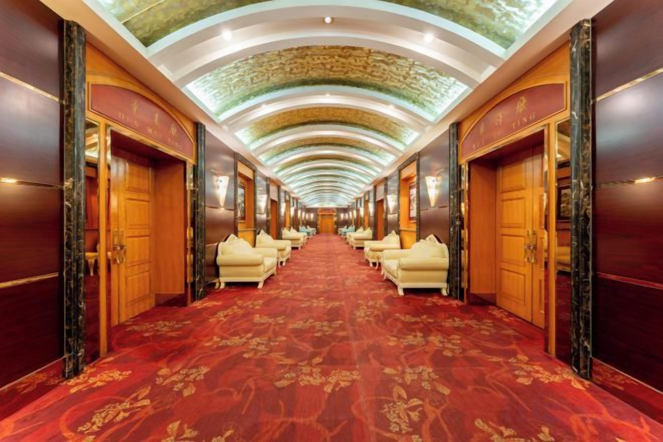 Un pasillo de hotel con alfombra roja, puertas de madera y zonas de estar.