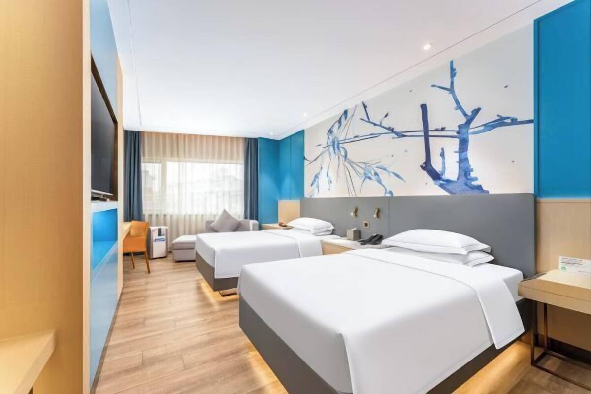 A hotel room with two beds, a desk, a chair, a window with curtains, and a wall art piece.
