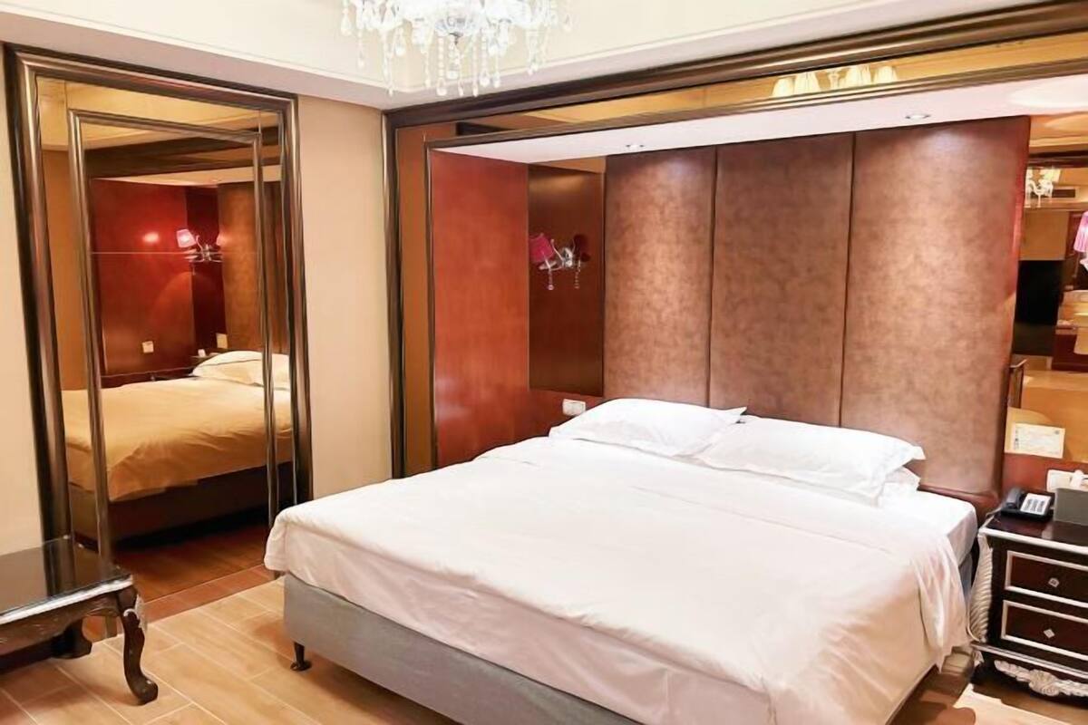 A hotel room with a large bed, a wardrobe with a mirror, and a bedside table.
