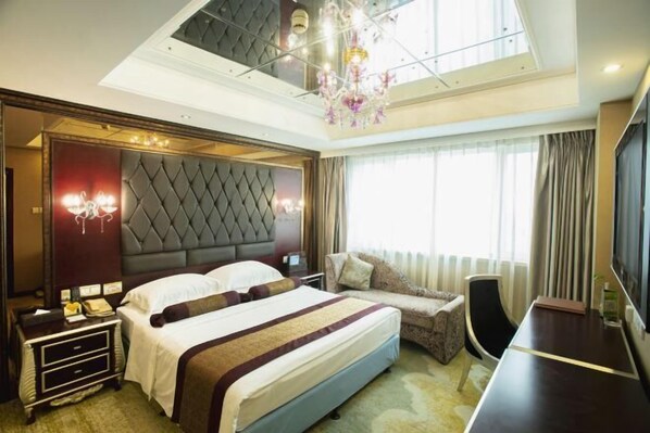 A modern hotel room with a large bed, a sofa, a desk, and a TV.