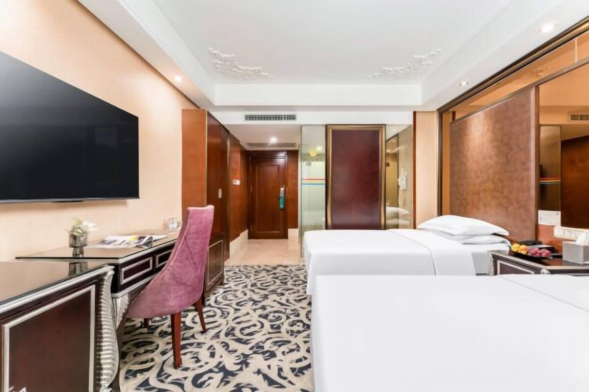 A hotel room with a bed, a desk, a chair, a television, and a large mirror.