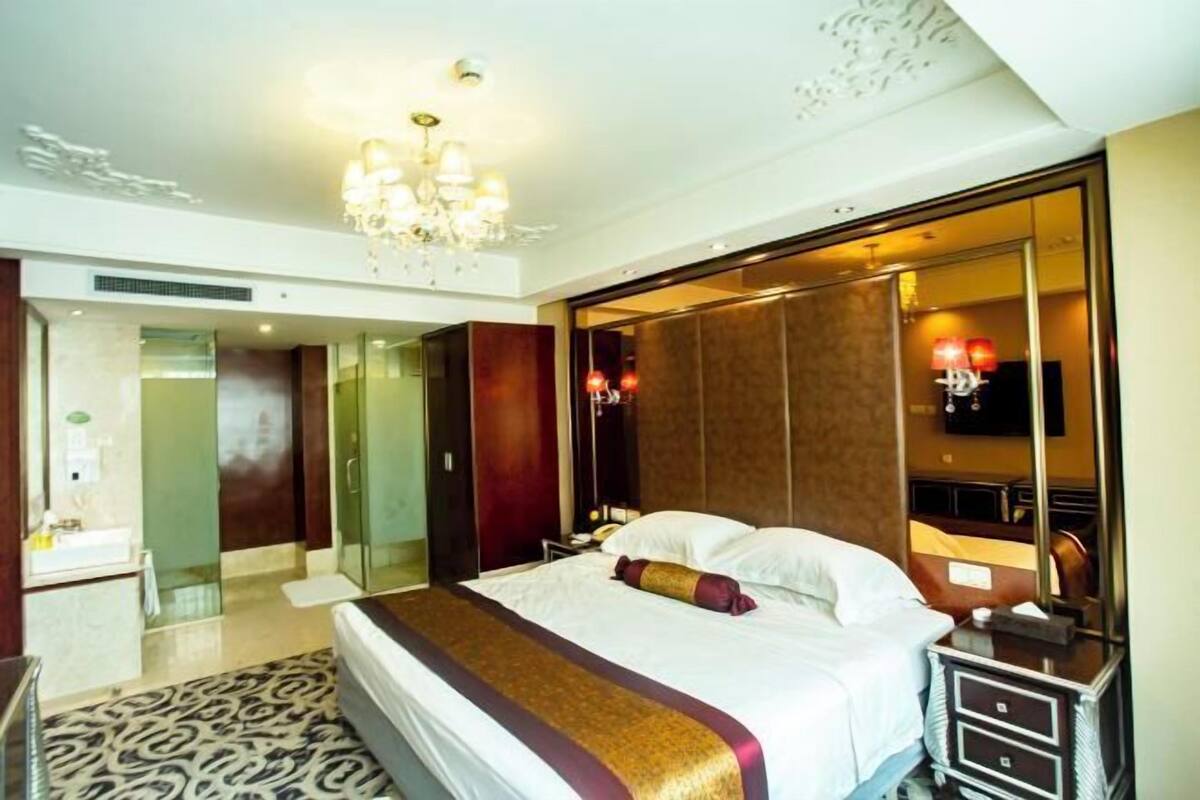 A hotel room with a large bed, a chandelier, a mirror, and a television.