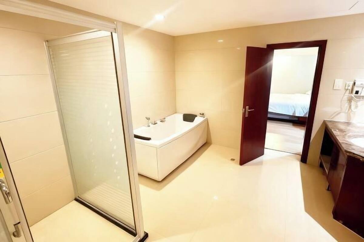 A modern bathroom with a bathtub, a shower enclosure, and a door leading to a bedroom.