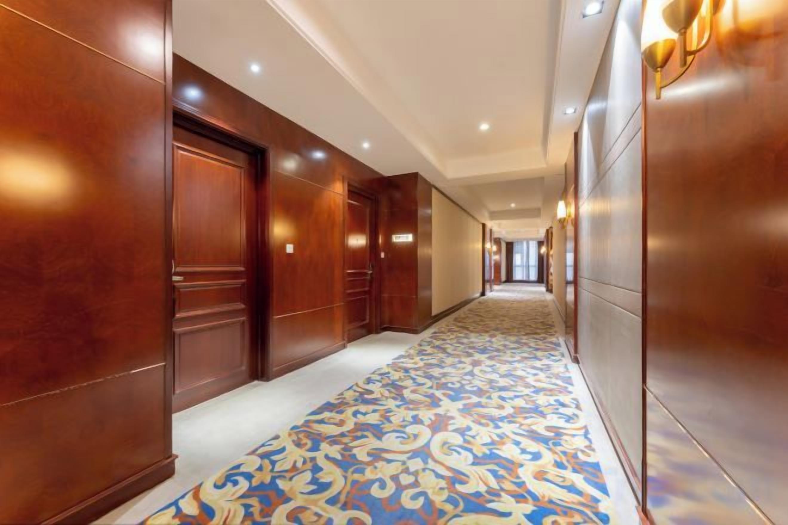 A hotel corridor with wooden doors, a patterned carpet, and recessed lighting.