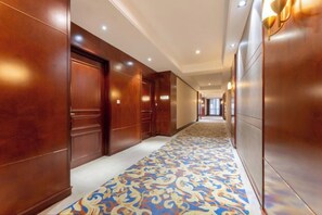 A hotel corridor with wooden doors, a patterned carpet, and recessed lighting.