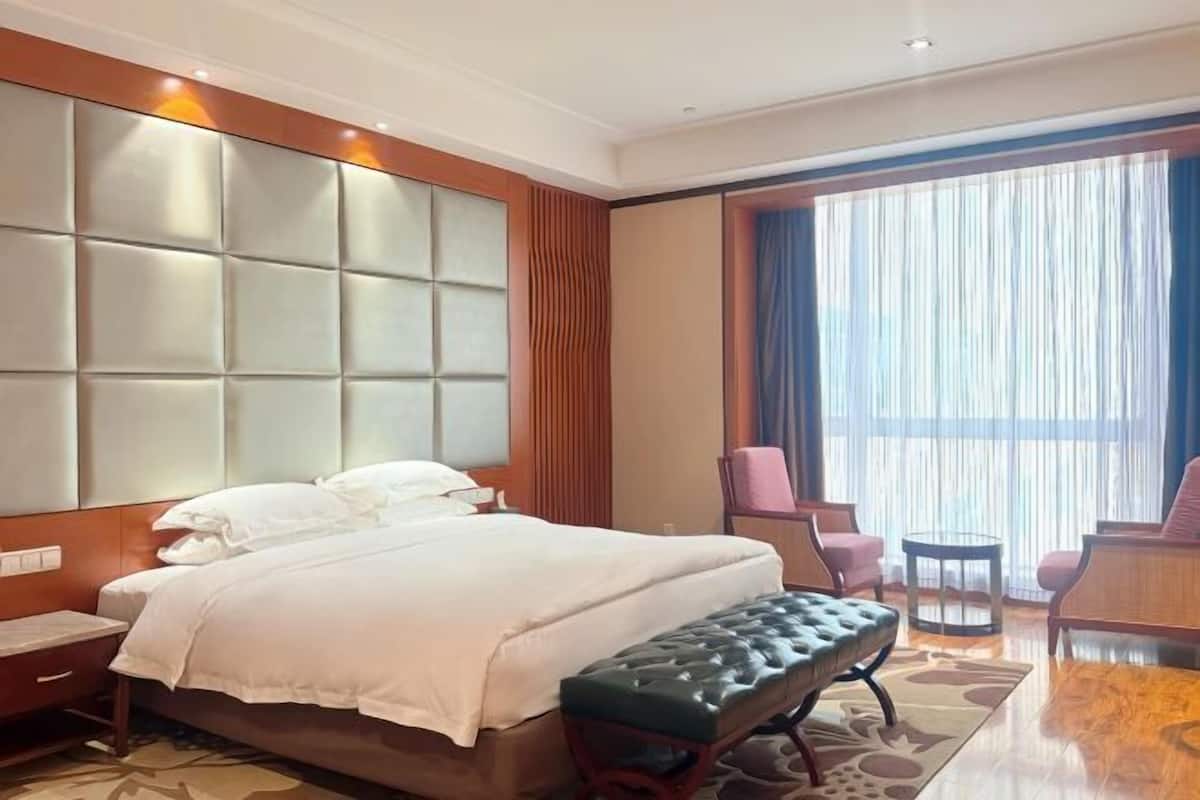 A hotel room with a large bed, a bench, a desk, and a chair.